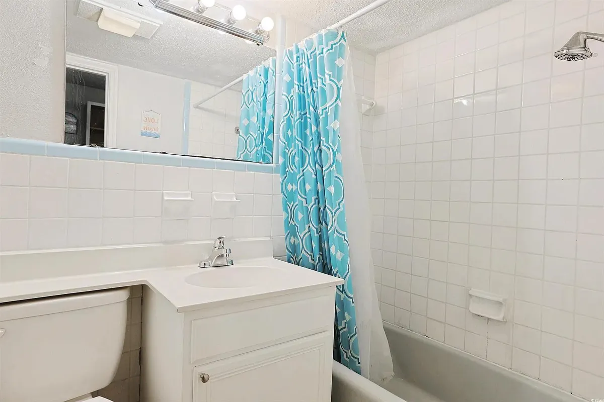 The bathroom area features a fresh, spa-like design with a white vanity, a blue shower curtain, and a bright mirror reflecting natural light. The space feels inviting and well-maintained, providing a private retreat for personal care and relaxation.