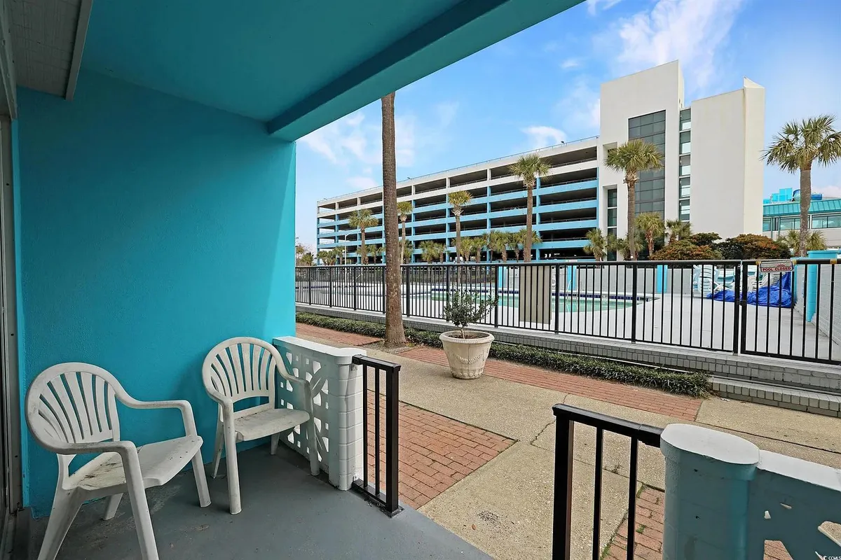 This image features a lively exterior pool area framed by blue walls and dotted with white chairs and palm trees. The swimming pool is front and center, inviting guests to take a dip or lounge nearby. Friends are shown socializing around the pool, capturing the resort’s casual, community-oriented vibe. Sunlight and natural greenery enhance the inviting atmosphere.